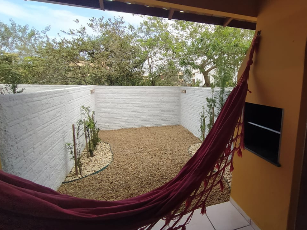 Área externa com rede pendurada entre árvores, mesa com cadeiras e vegetação ao redor; ambiente tranquilo para relaxar