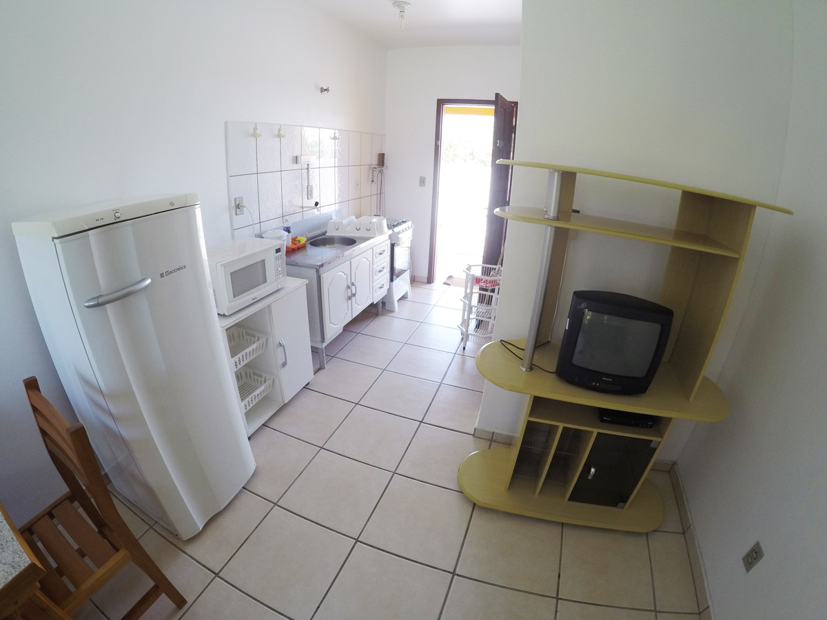 Mesa de jantar para quatro pessoas em madeira clara junto à cozinha, cadeiras estofadas e parede decorada; ambiente convidativo para refeições